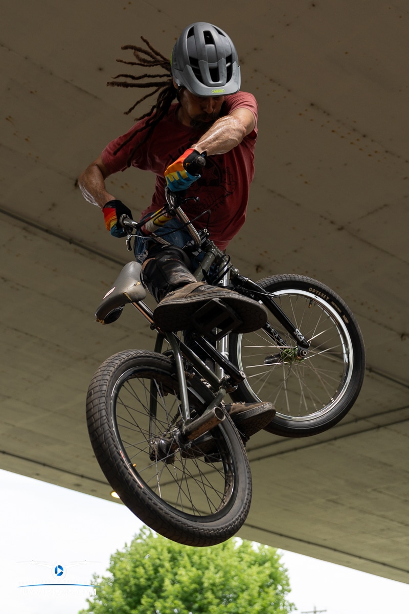 A BMX rider with dreadlocks performs an aerial trick under a bridge at the Charleston Sternwheel Regatta 2023.