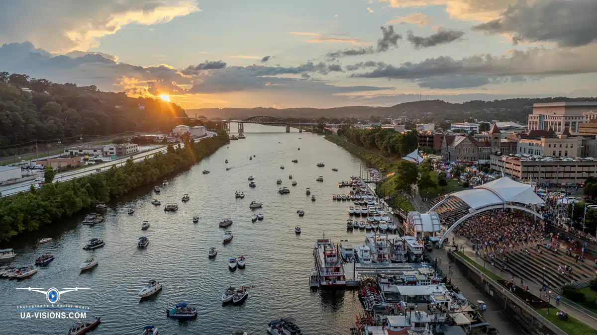 Aerial view of a city at sunset, with boats dotting a tranquil river. Silhouetted buildings rise against the golden sky, creating a harmonious blend of nature and urban life.
