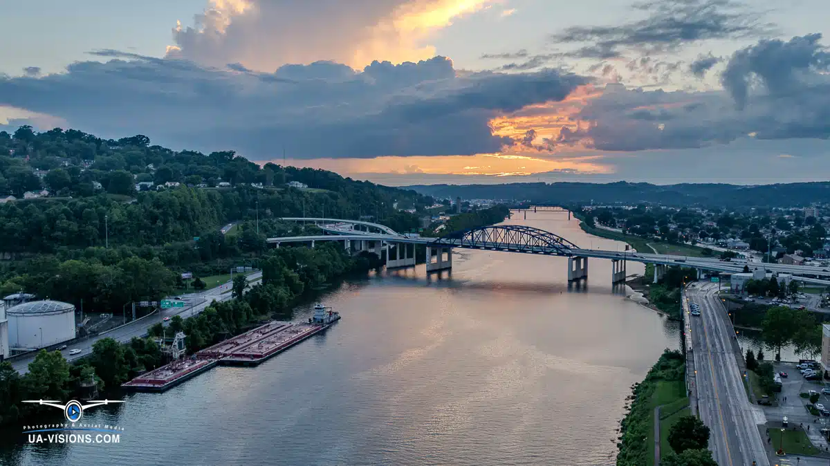 Aerial view of a bridge spanning a river, bathed in sunset's golden glow. A plane soars above, while a boat glides below, capturing nature and human marvels in harmony.