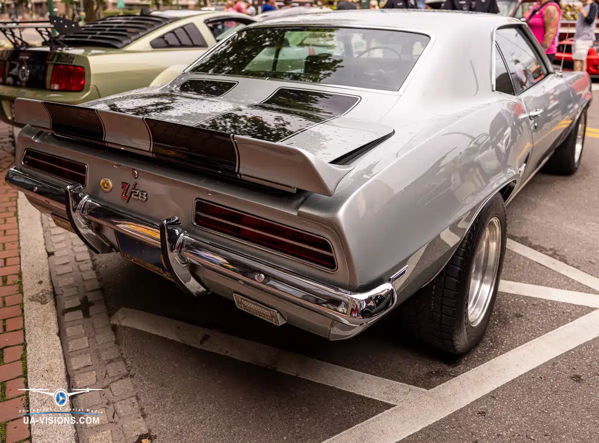 Dive into a vibrant urban setting where classic cars take center stage. A sleek silver Chevrolet Camaro stands out, parked in a lot