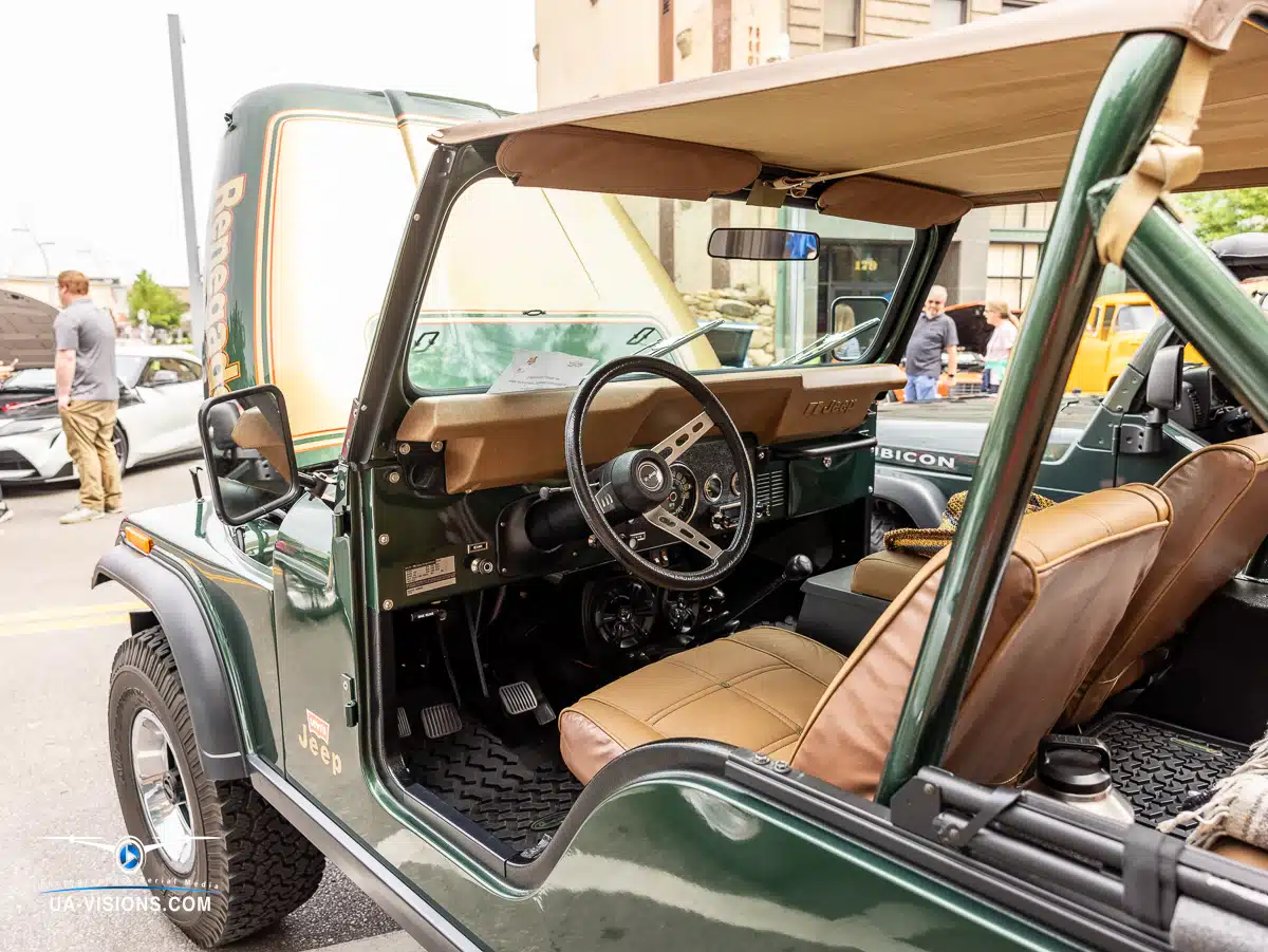Green Jeep in the spotlight with enthusiasts admiring its design and mechanics at an automotive event.