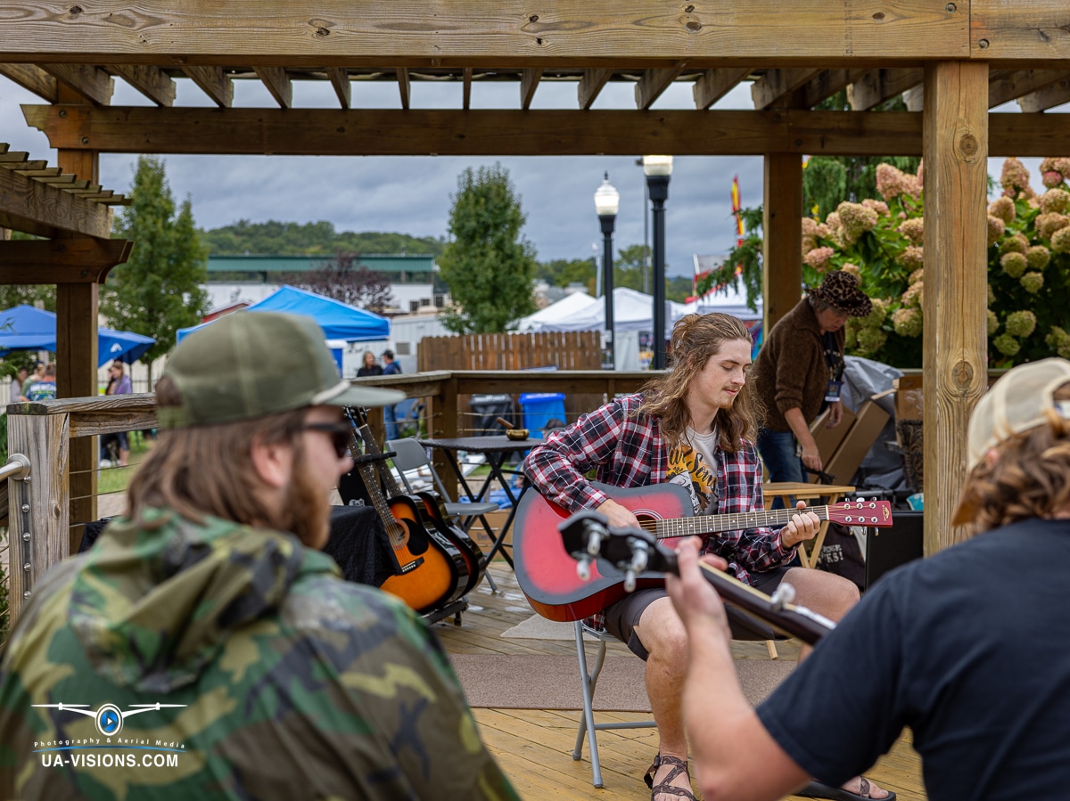 Musicians in casual attire playing guitars on a wooden deck at the Healing Appalachia event.