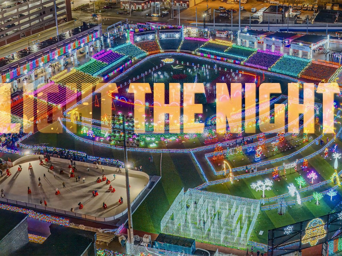 Aerial view of vibrant 'Light the Night' event with colorful illuminated letters against the evening city backdrop.