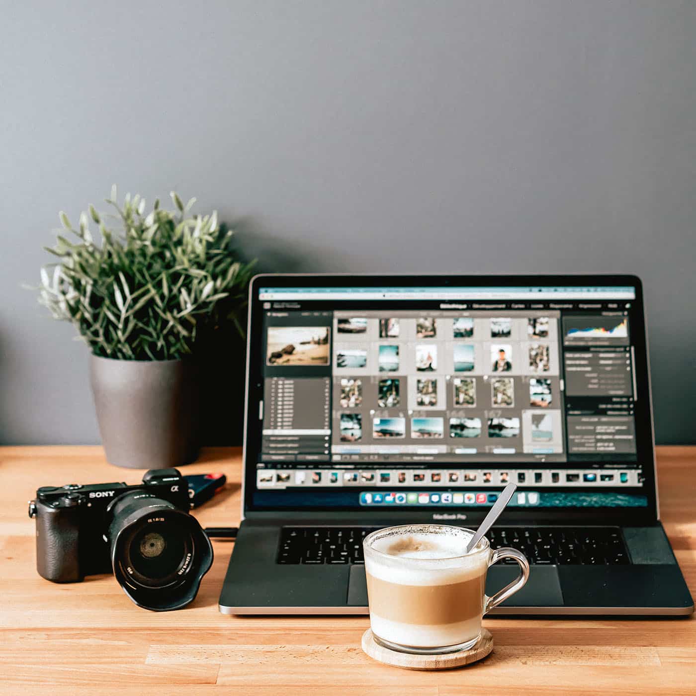 Professional photo editing workspace with a laptop displaying photo management software, a Sony camera, and a cup of coffee on a wooden desk.
