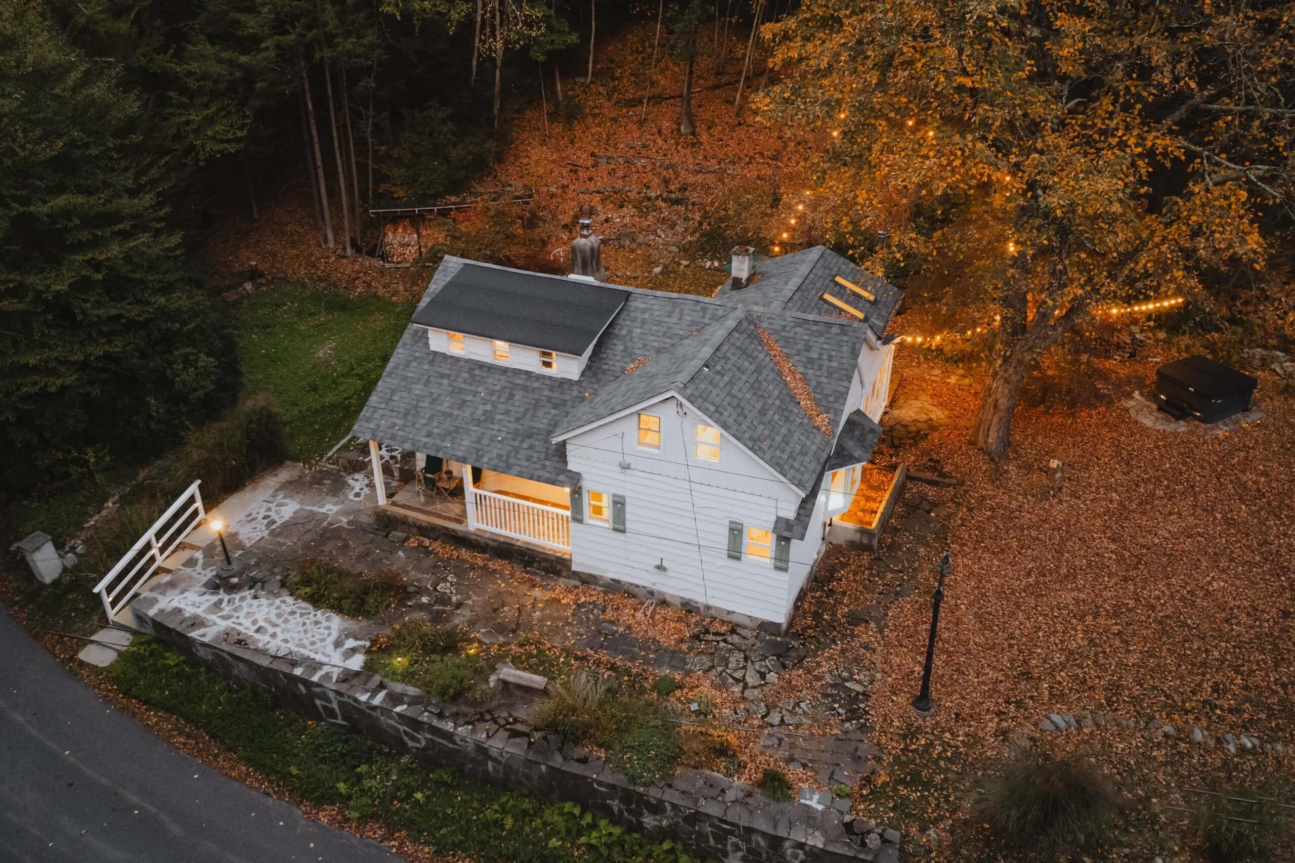 Aerial view of a picturesque house in autumn with a cozy fire pit and a solitary figure enjoying the tranquil evening.