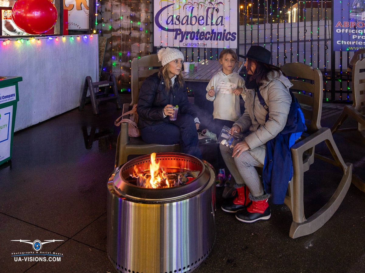 This heartwarming scene by UA-Visions at Charleston's Light the Night captures a family's intimate moment by the fire, reflecting the warmth and charm of holiday gatherings, perfect for family-friendly event promotion.