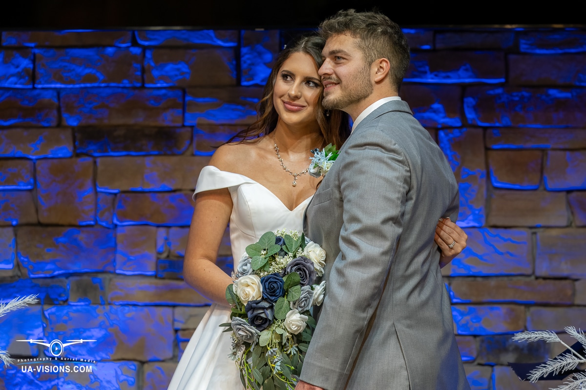 Bride and groom Kaitlyn and Logan Gaddy sharing a smile with a blue stone backdrop.