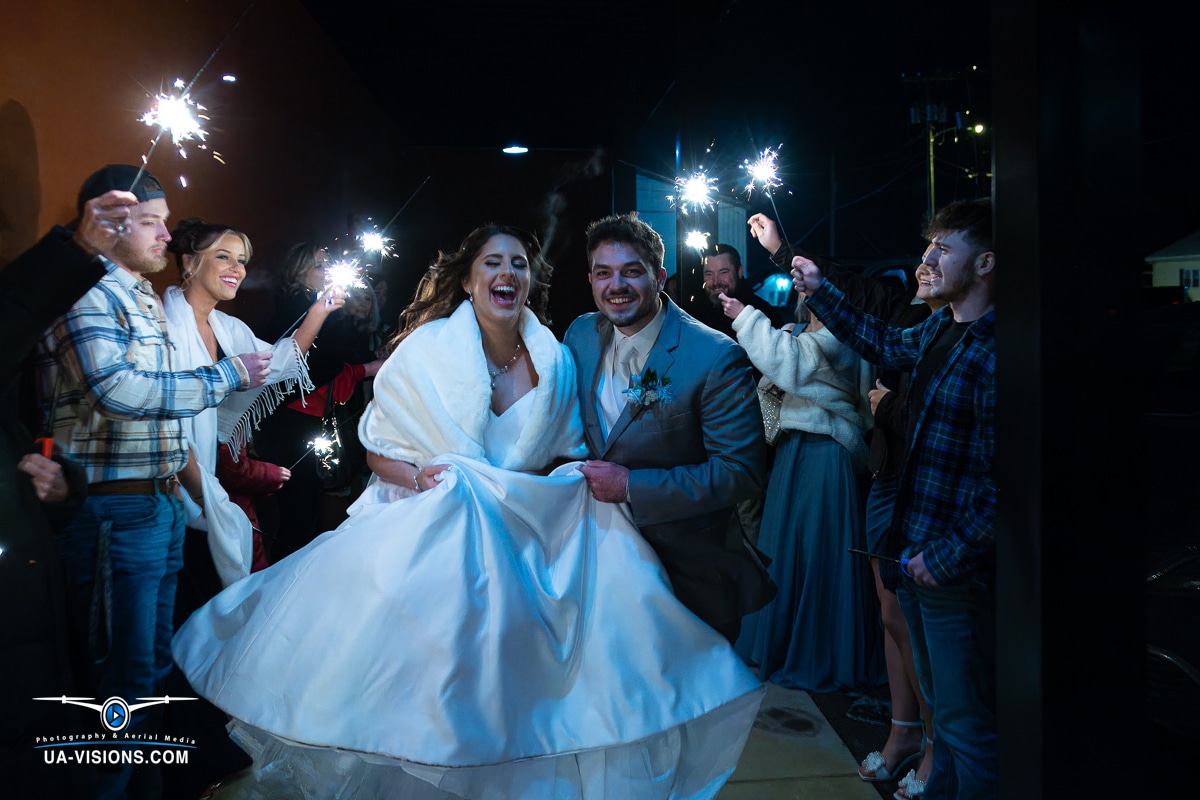 Newlyweds Katilyn and Logan Gaddy laugh as they pass through a tunnel of sparklers held by guests at their wedding in Hurricane, WV.