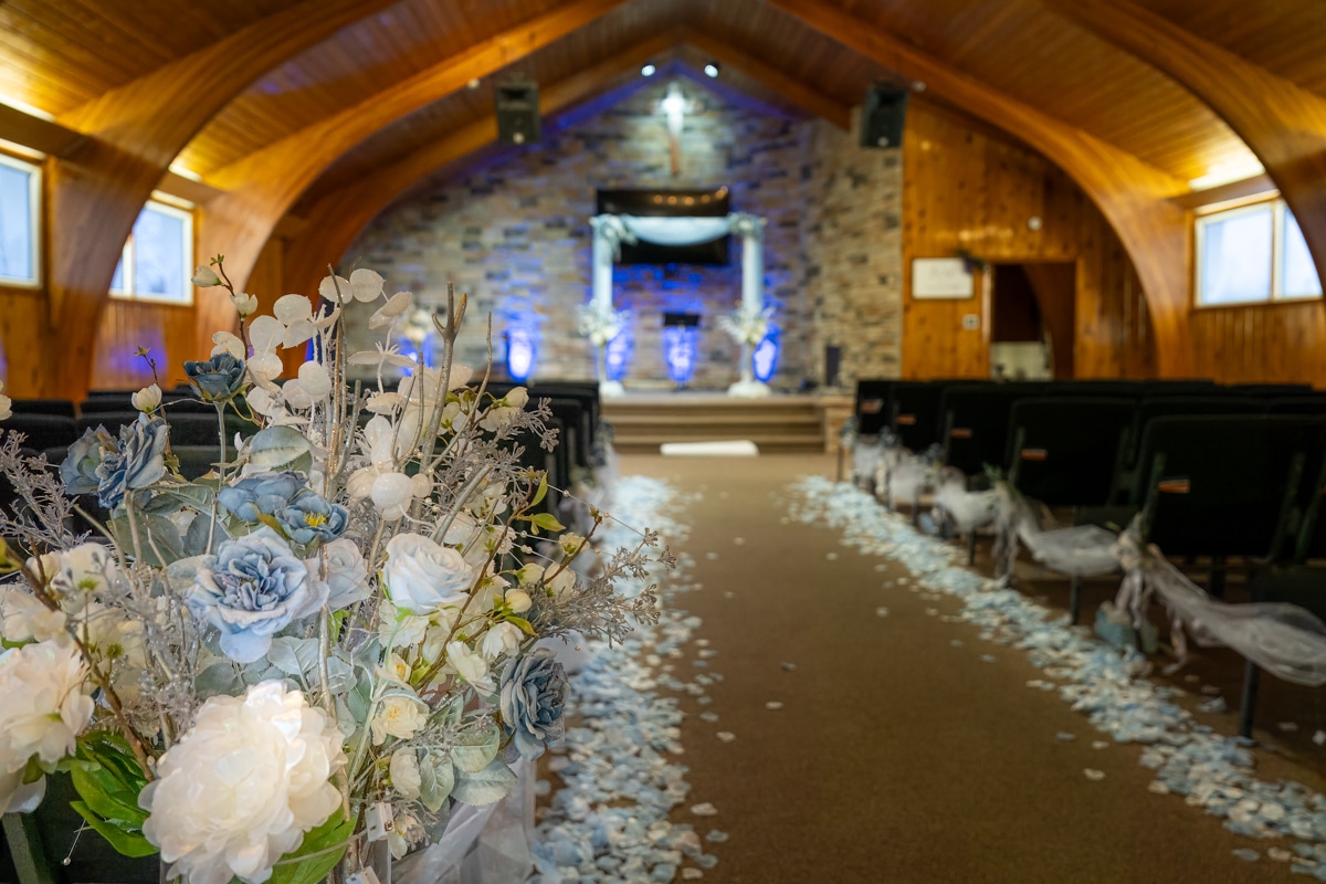 Aisle of a wedding chapel decorated with blue and white flowers leading to the altar.