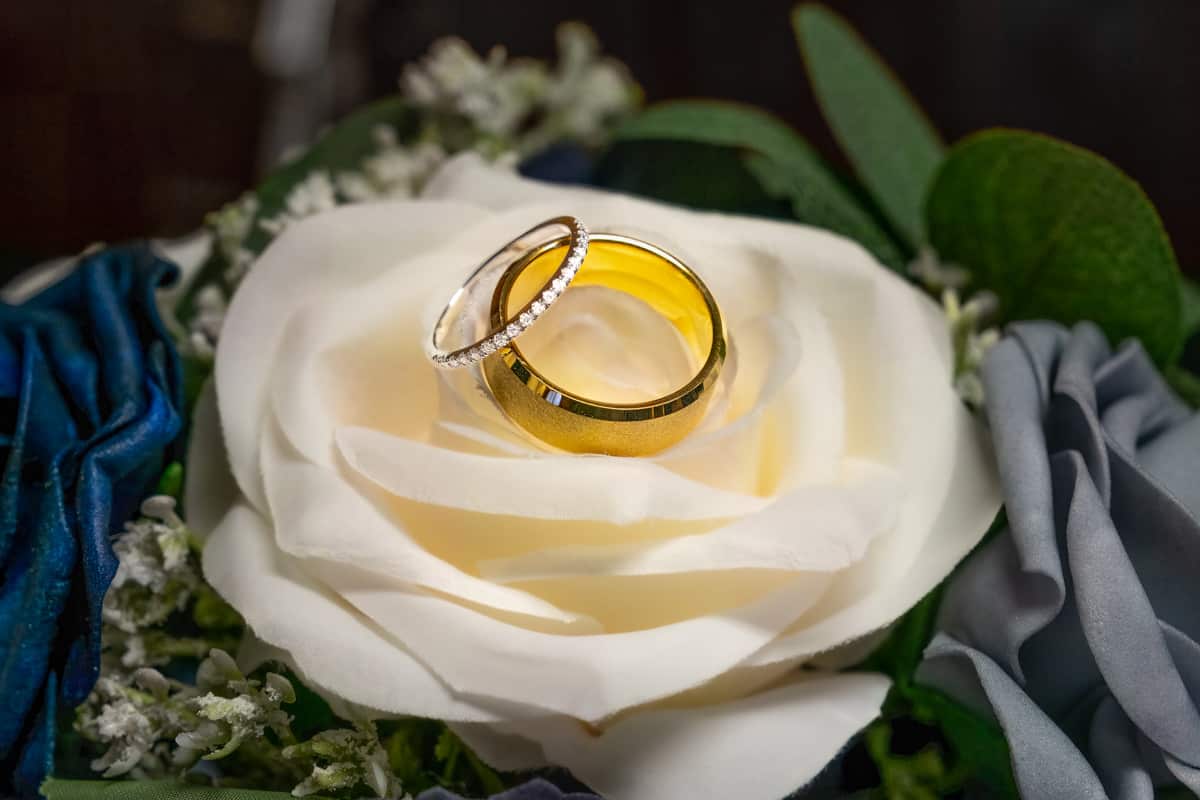 Gold and diamond wedding rings on a white rose petal.