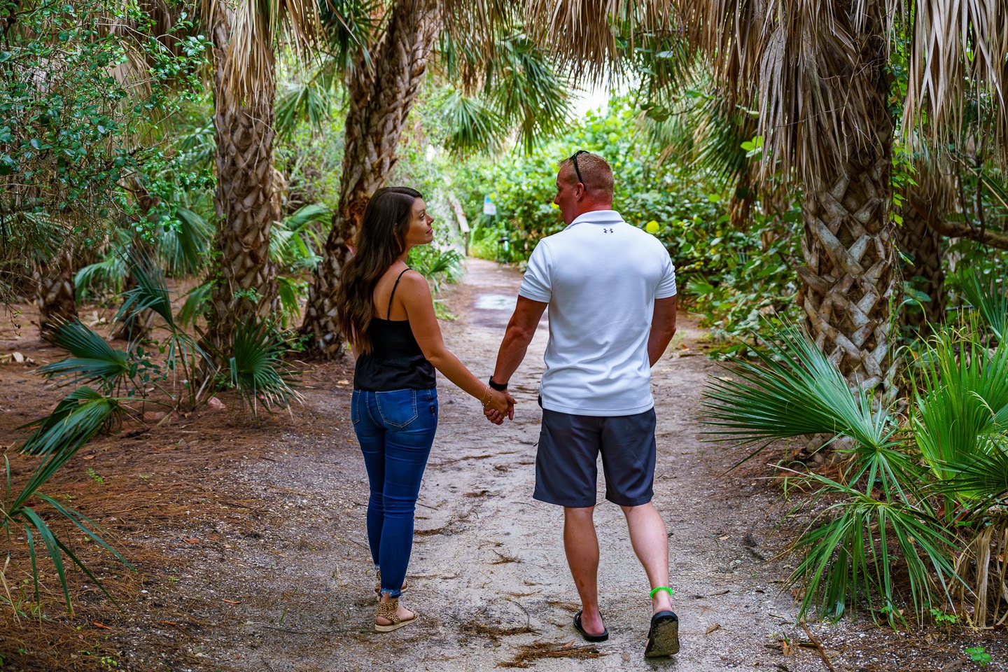 Couple holding hands on a serene nature trail surrounded by lush palms.