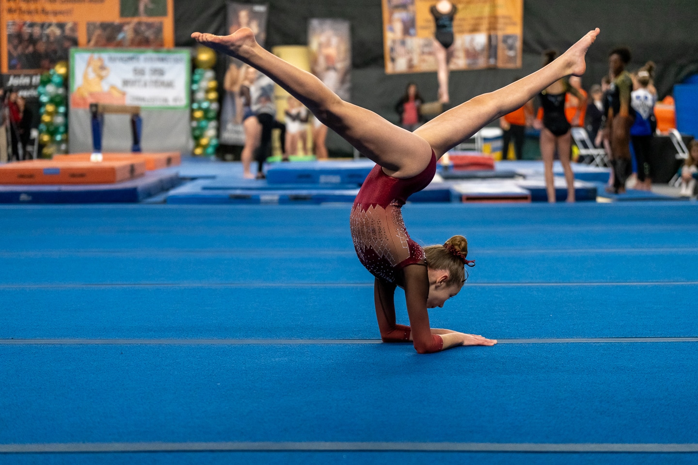 Young gymnast performing a handstand on the floor exercise mat at a gymnastics competition.