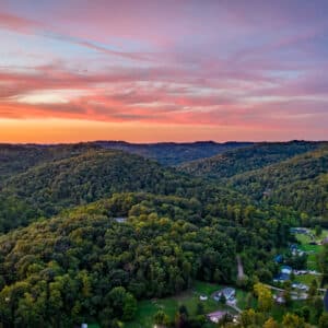 Sunset Over an Emerald Forest | An aerial view captures a dense forest bathed in the warm glow of a sunset. The landscape showcases a rich tapestry of trees reaching towards the horizon, offering a tranquil and breathtaking vista.