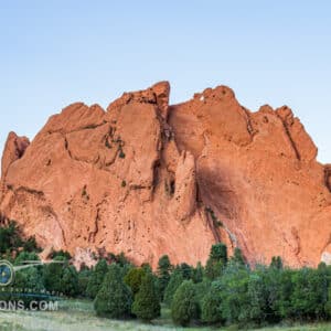 Early morning light on a dramatic red sandstone rock formation surrounded by greenery.